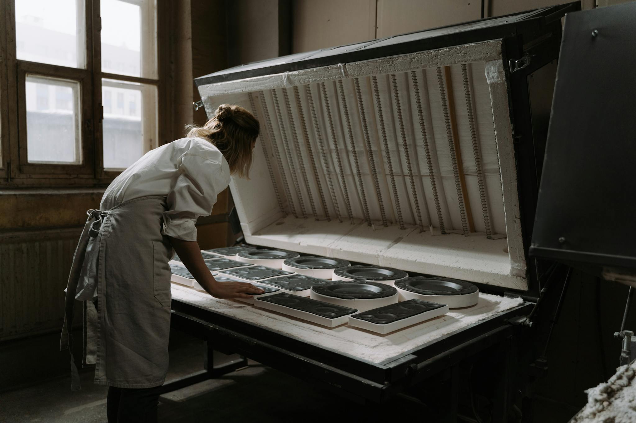 A female artisan carefully arranges ceramics in an industrial kiln, indicating precision and craftsmanship.