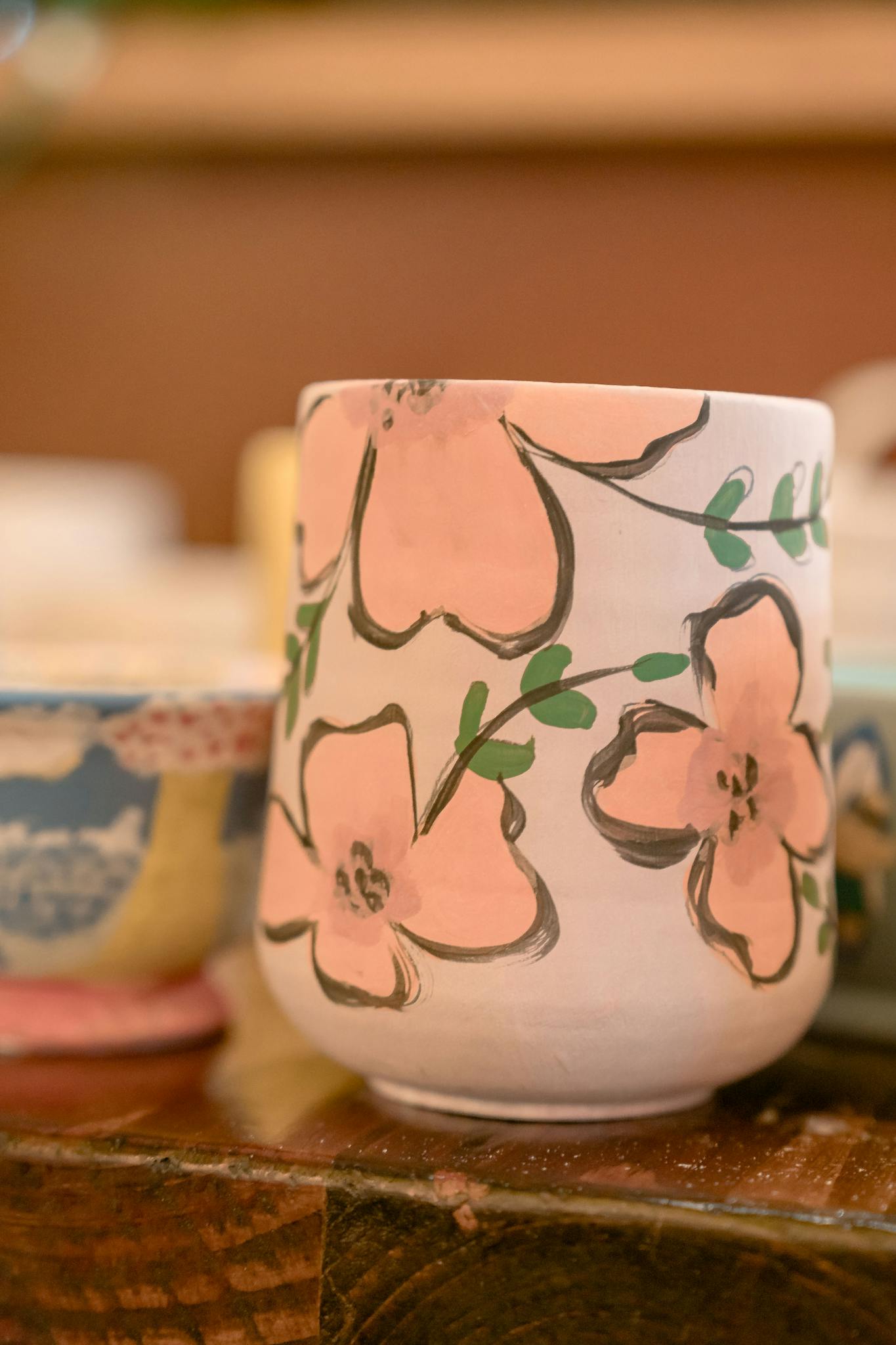 Artistic handmade ceramic cups featuring floral designs on a workshop table.