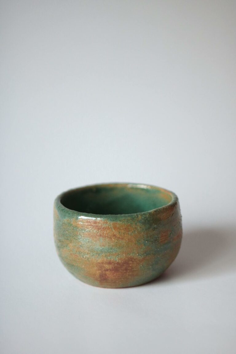 Close-up of a handcrafted ceramic cup with a glazed finish, against a soft backdrop.