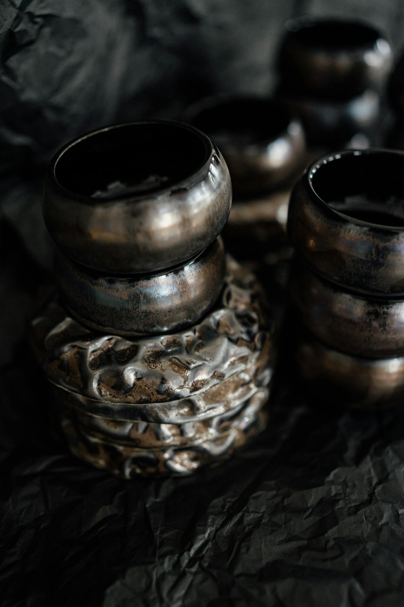 Close-up of stacked handcrafted metallic finish ceramic bowls on a textured dark background.