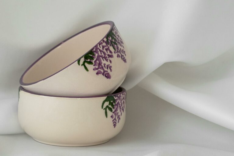 Stacked handmade painted bowls featuring floral designs on a soft white fabric background. Perfect for home decor.